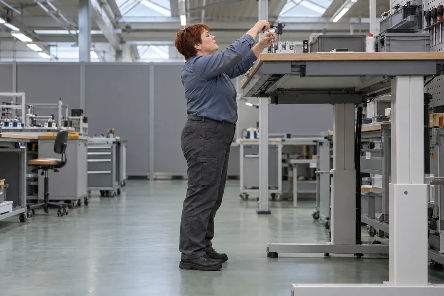 Opératrice debout, bras au-dessus des épaules et nuque en extension, plan de travail haut